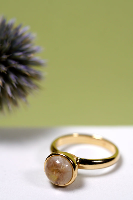 Gold ring with a  quartz round stone on a white surface with a green background