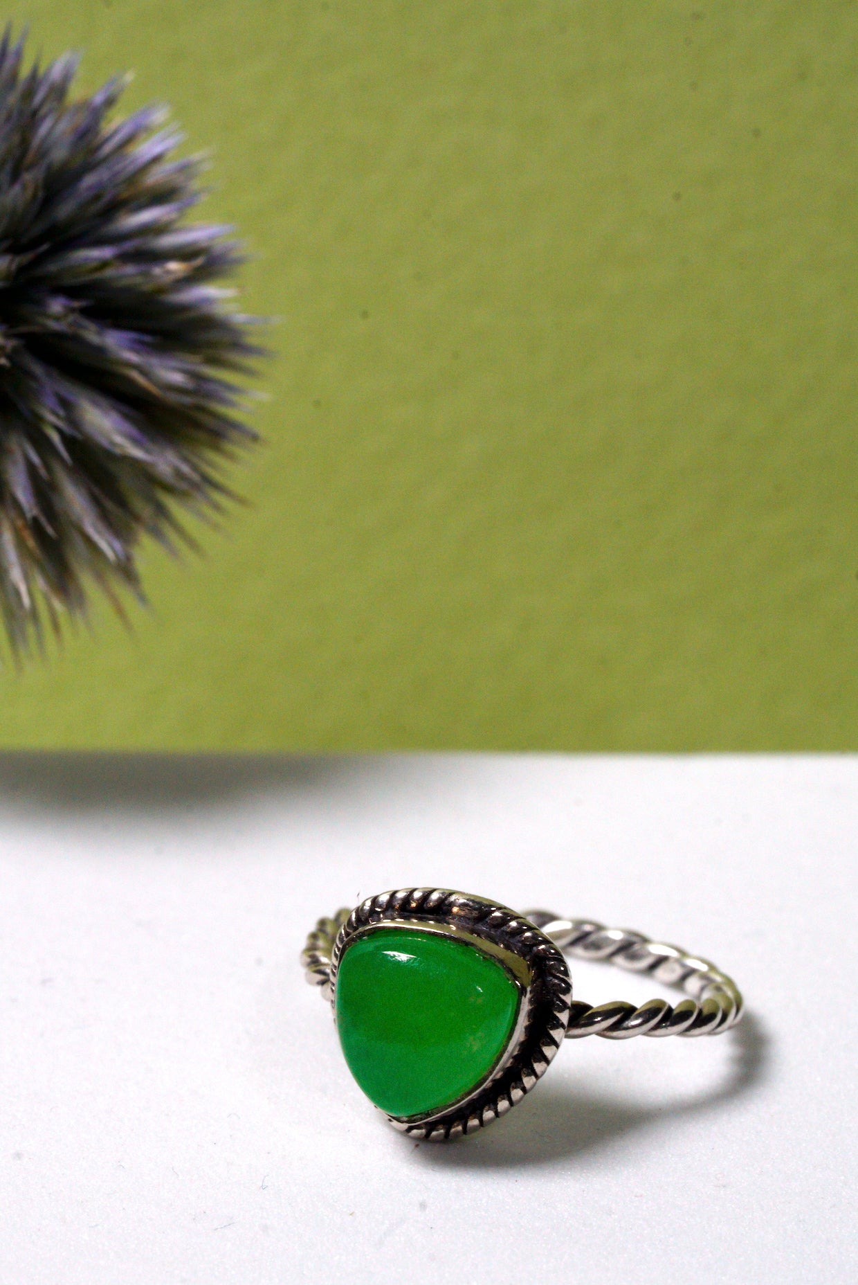 Green jade ring with silver band on a white surface with a green background