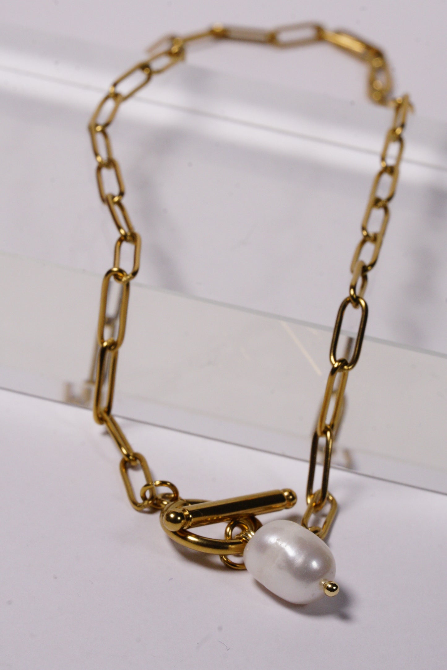 Gold paperclip chain bracelet with a pearl on a white background
