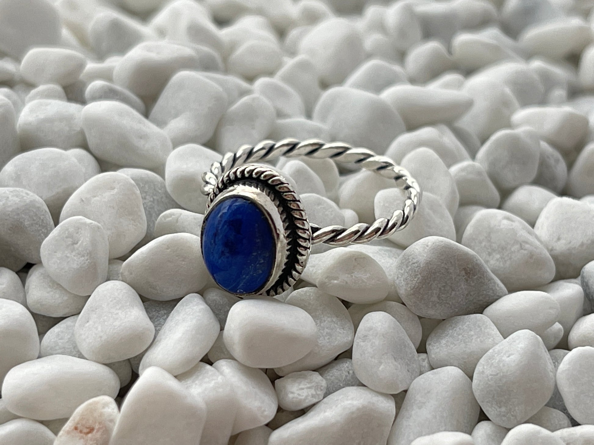 Silver ring with a lapis lazuli gemstone on white pebbles
